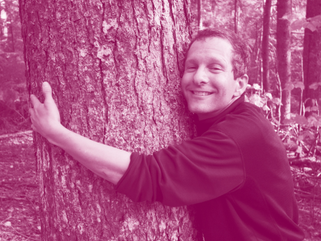 man wearing black shirt smiling as he hugs tree