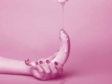 woman with painted nails holding banana with lube drizzling over it 