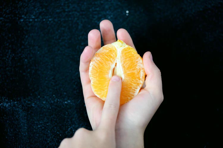 A halved orange with a finger pressed near the middle, representing a vagina.